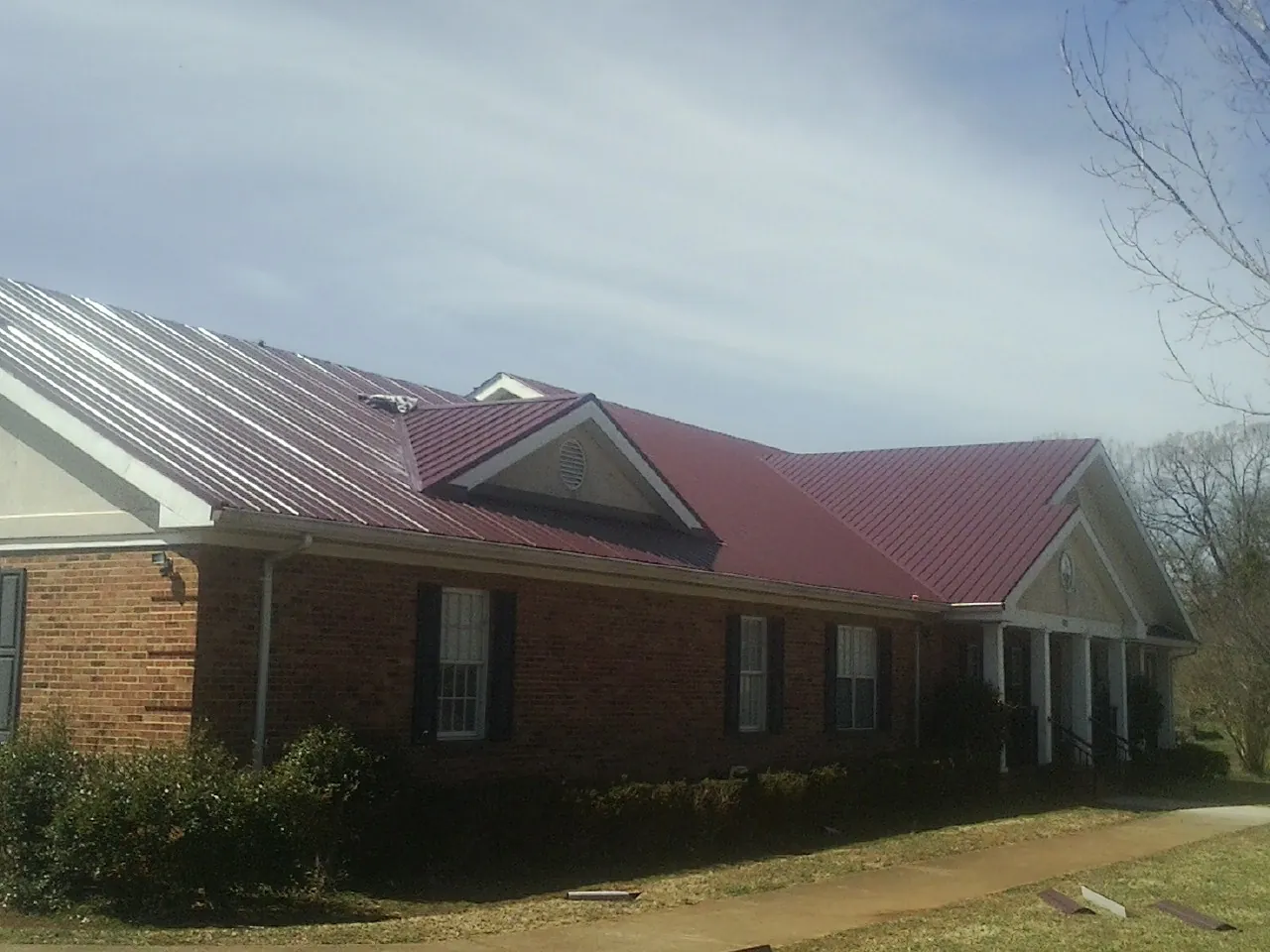 Red metal roof with gabled entries on a long brick building, from a Hail Damage Roof Repair job in Stoystown