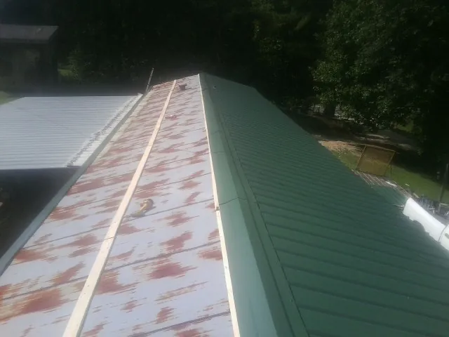 Old rusted panels beside newly installed green metal roofing — Wind Damage Roof Repair by Roofing Brothers in Stoystown
