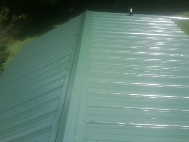 New green metal panels meeting at the ridge of a roof — Flat Roof Repair work by our crew in Stoystown