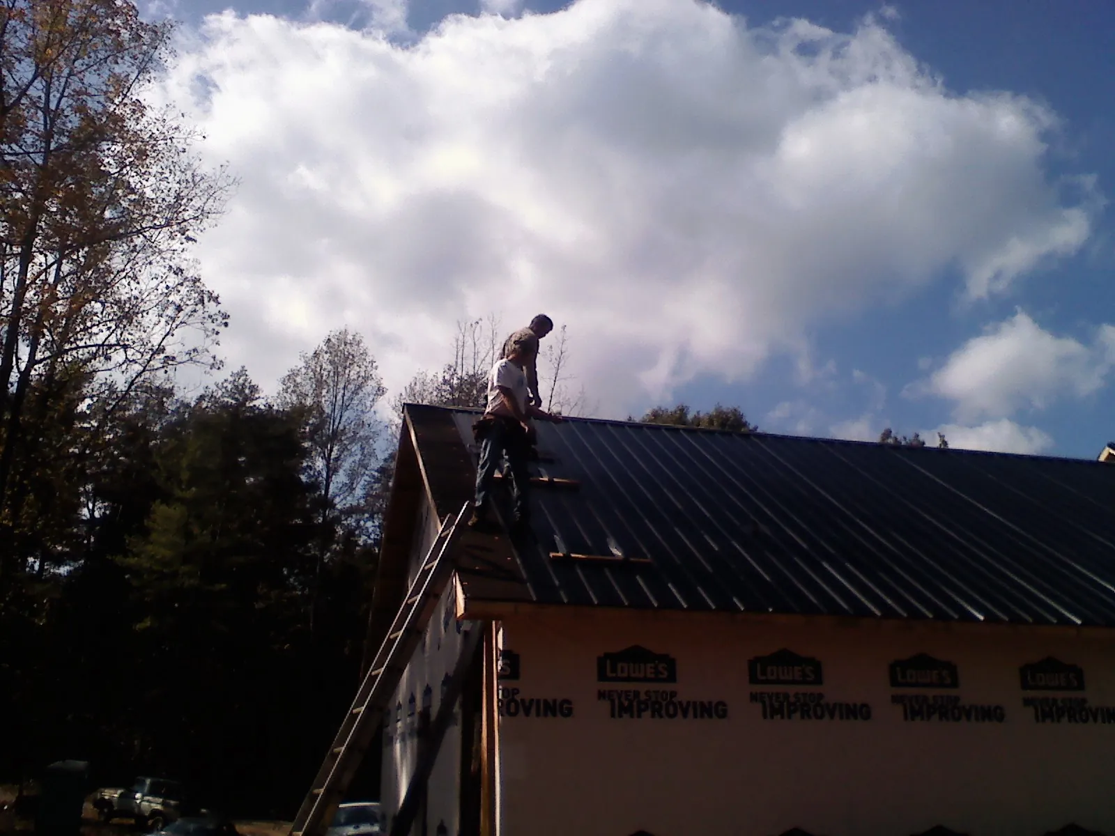 Roofer fastening dark metal panels high against a cloudy sky, from a Roof Inspection job in Stoystown