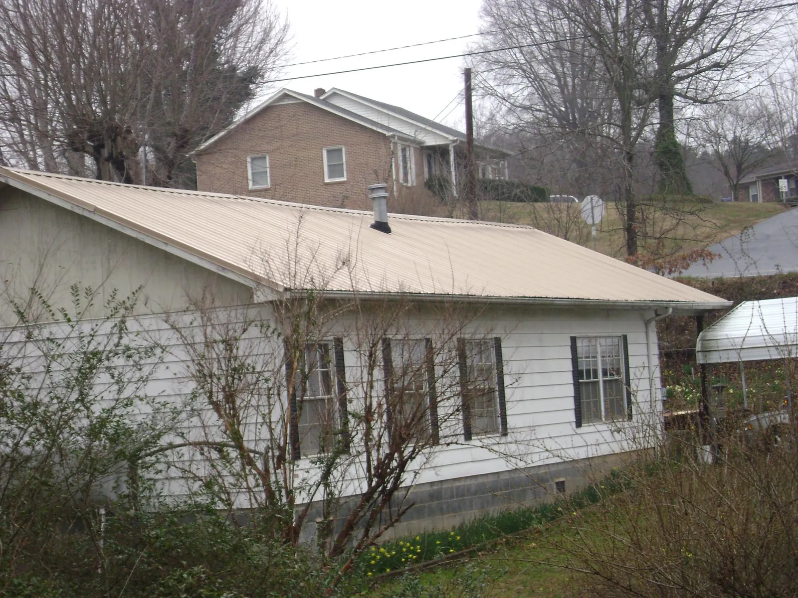 Tan metal roof on a white sided house set into a hillside — Commercial Roofing by Roofing Brothers in Stoystown
